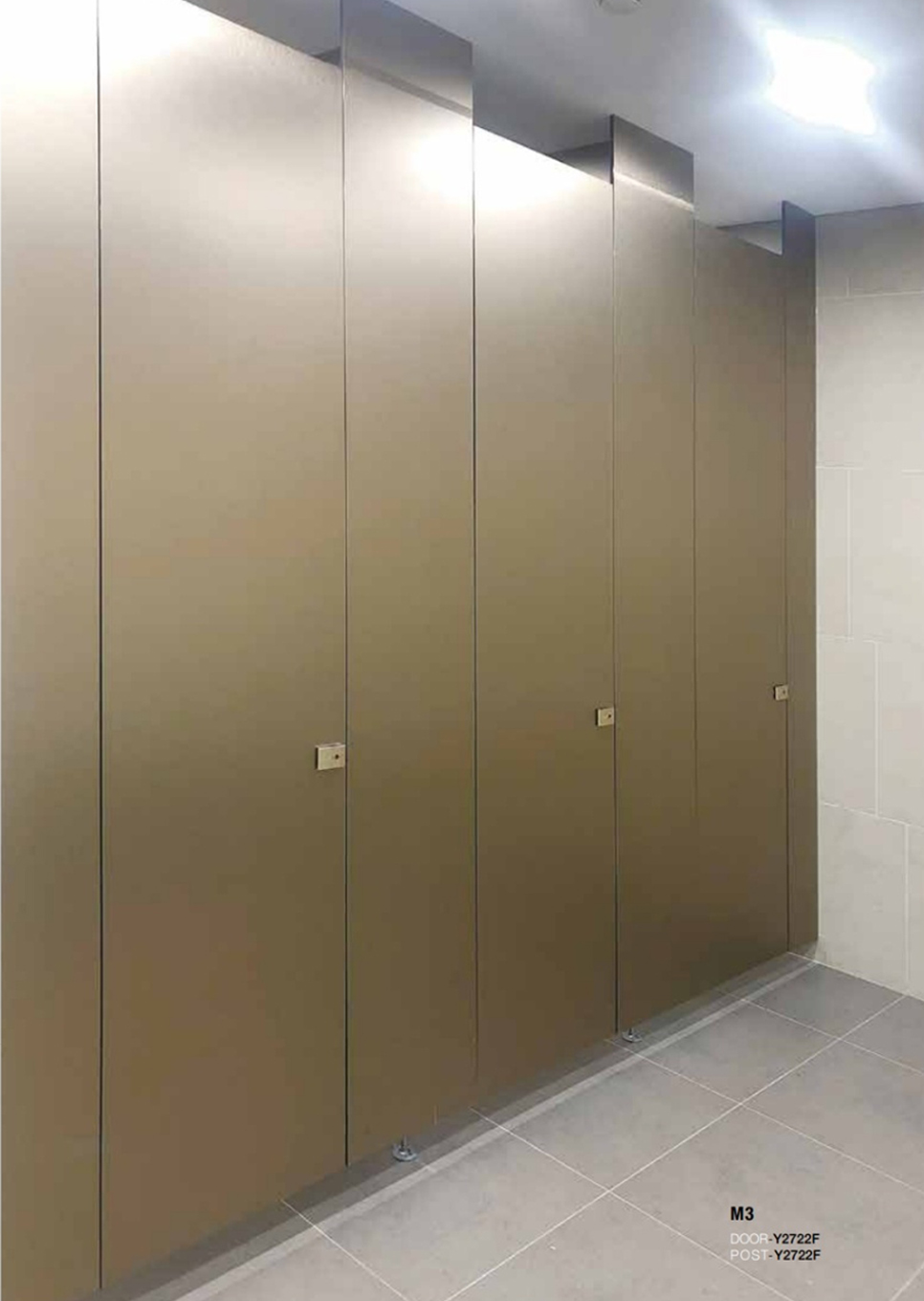 Row of brown metal restroom stalls with closed doors in a public bathroom, beige tiles and gray floor visible.